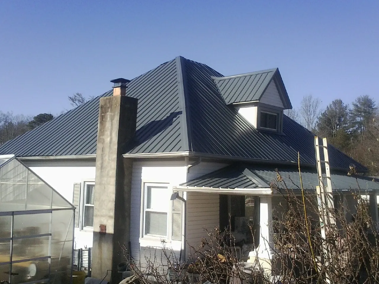 Dark blue standing seam metal roof on a white farmhouse with dormer — Slate & Tile Roof Repair by Roofing Brothers in Rudd
