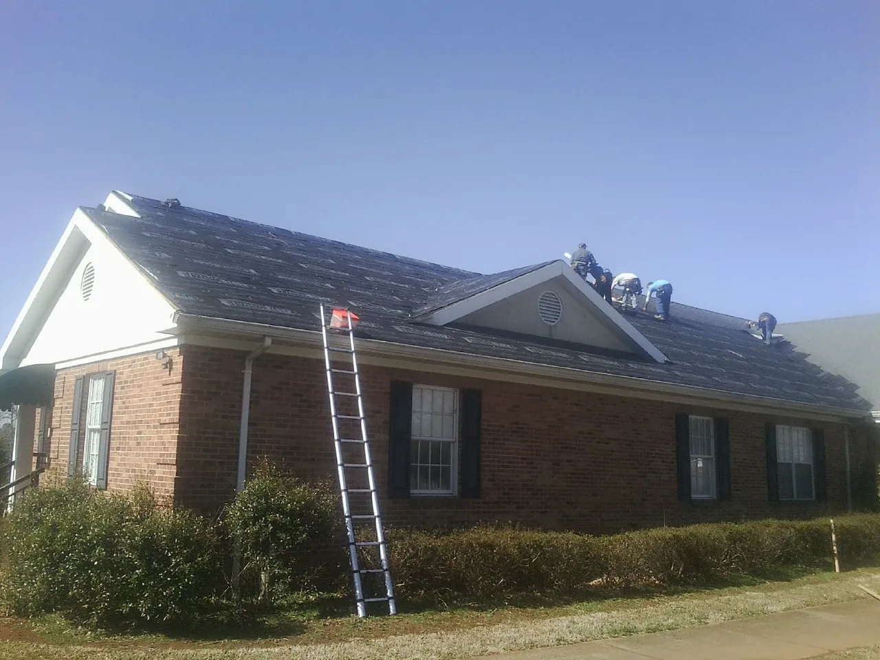 Crew tearing shingles off a brick ranch roof with a ladder set — Emergency Roof Repair work by our crew in Rudd