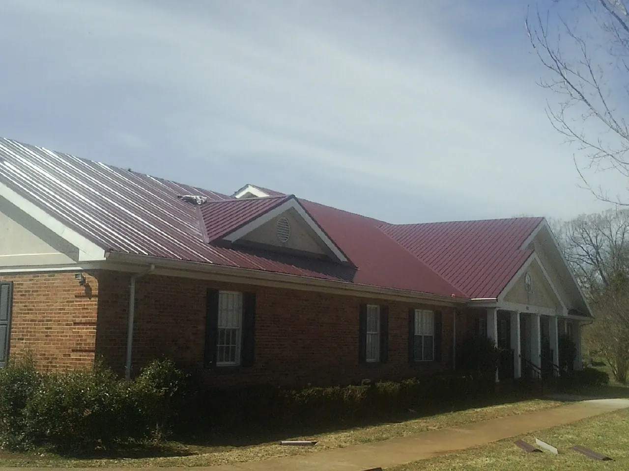Red metal roof with gabled entries on a long brick building, from a Hail Damage Roof Repair job in Rudd