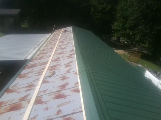 Old rusted panels beside newly installed green metal roofing — Wind Damage Roof Repair by Roofing Brothers in Rudd