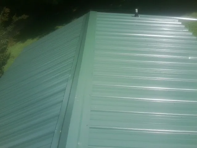 New green metal panels meeting at the ridge of a roof — Flat Roof Repair work by our crew in Rudd