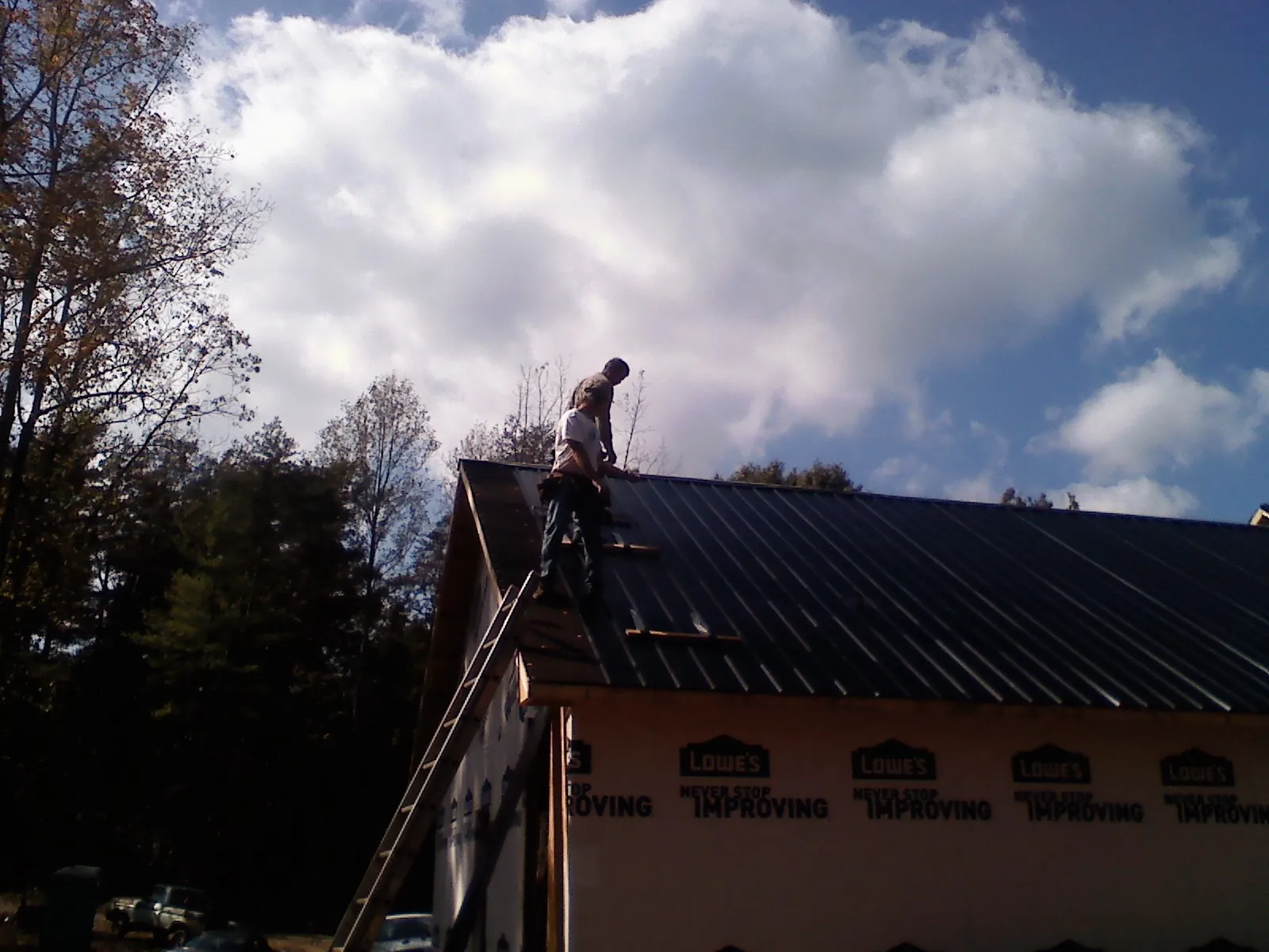 Roofer fastening dark metal panels high against a cloudy sky, from a Roof Inspection job in Rudd