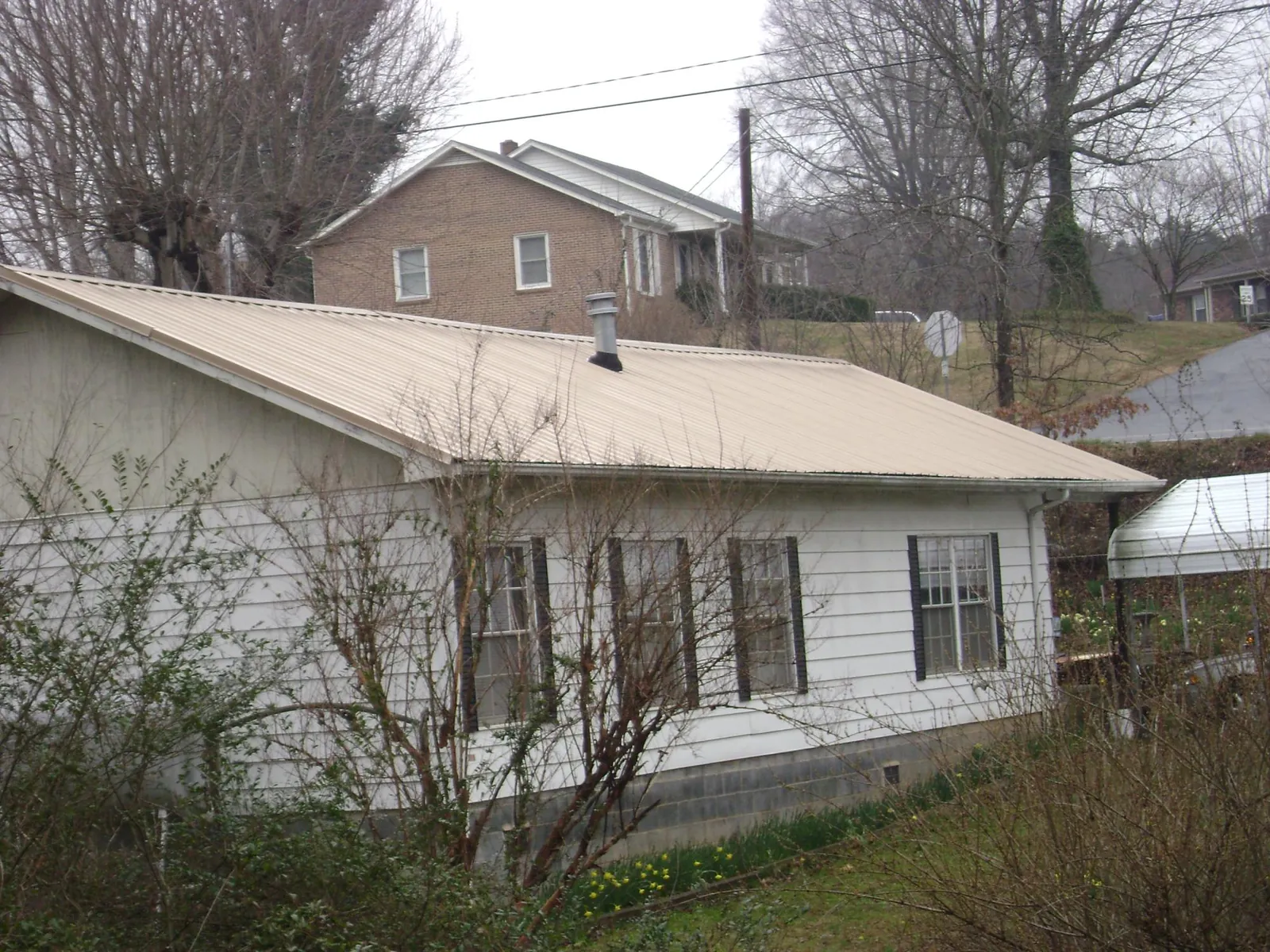 Tan metal roof on a white sided house set into a hillside — Commercial Roofing by Roofing Brothers in Rudd